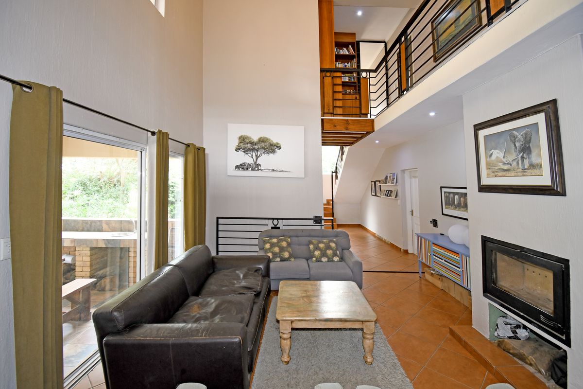 Spacious double-volume living area featuring a built-in fireplace, tiled flooring, and a mezzanine level overlooking the space with access to an outdoor patio.