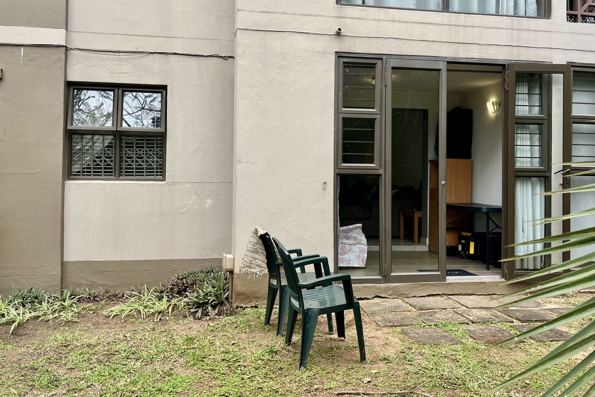 Rear exterior view of the apartment featuring aluminium framed windows and sliding doors leading to a small paved garden area.