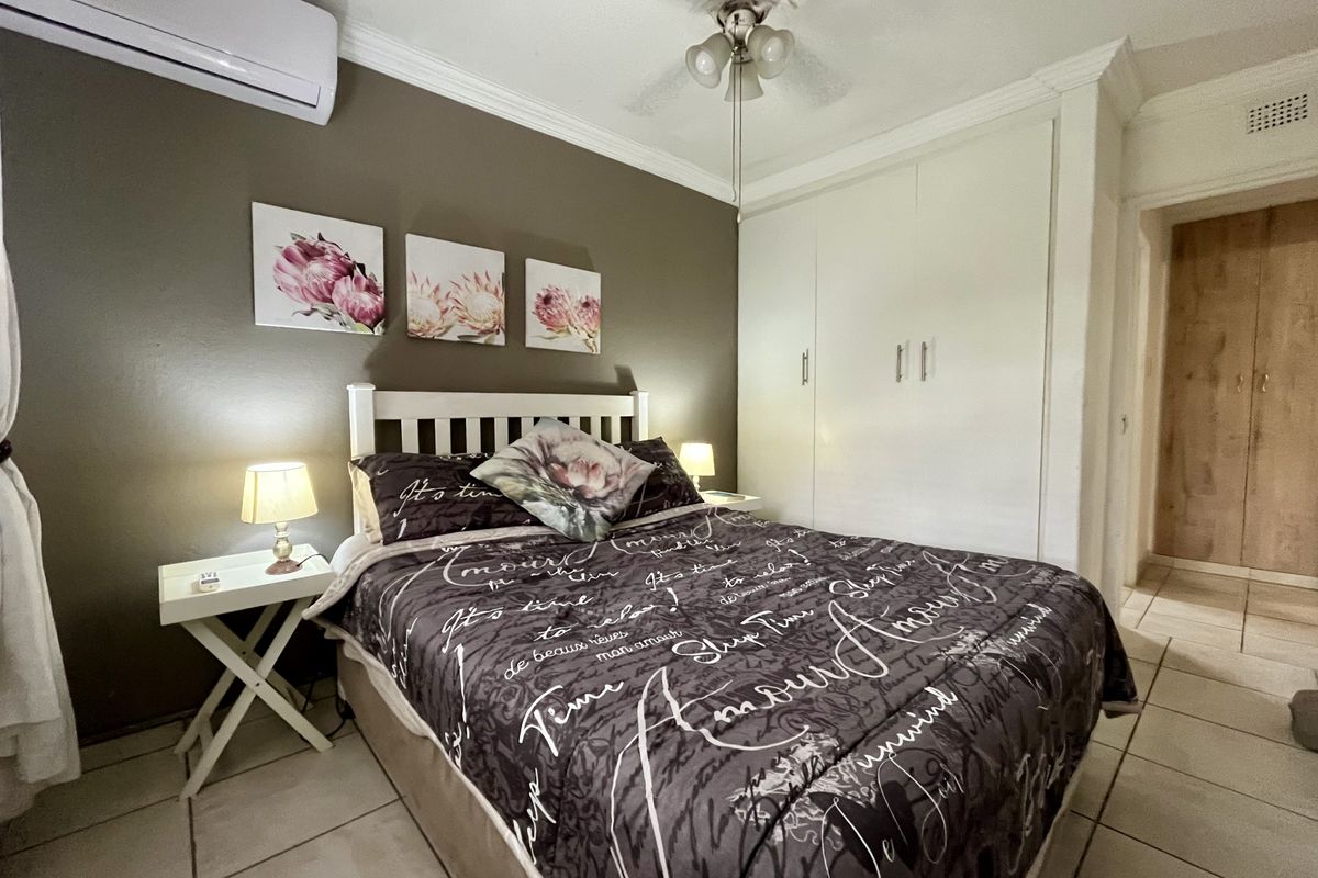 A well-maintained bedroom featuring built-in cupboards, tiled flooring, a ceiling fan, and a wall-mounted air conditioning unit.