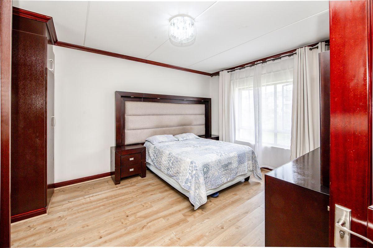 A well-lit bedroom featuring wood-look laminate flooring, dark wood trim, and a built-in wardrobe.