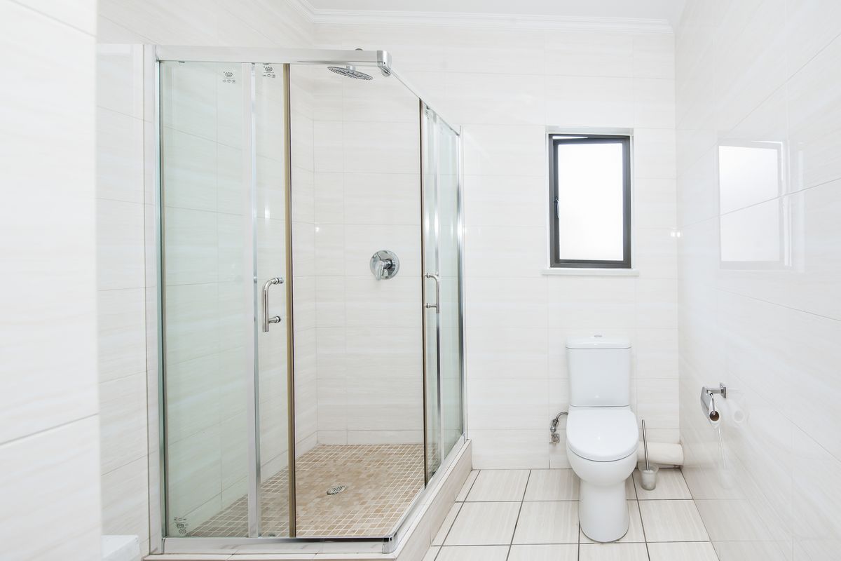 A clean, modern bathroom featuring a glass-enclosed shower with mosaic tile flooring, a white toilet, and neutral wall tiling.