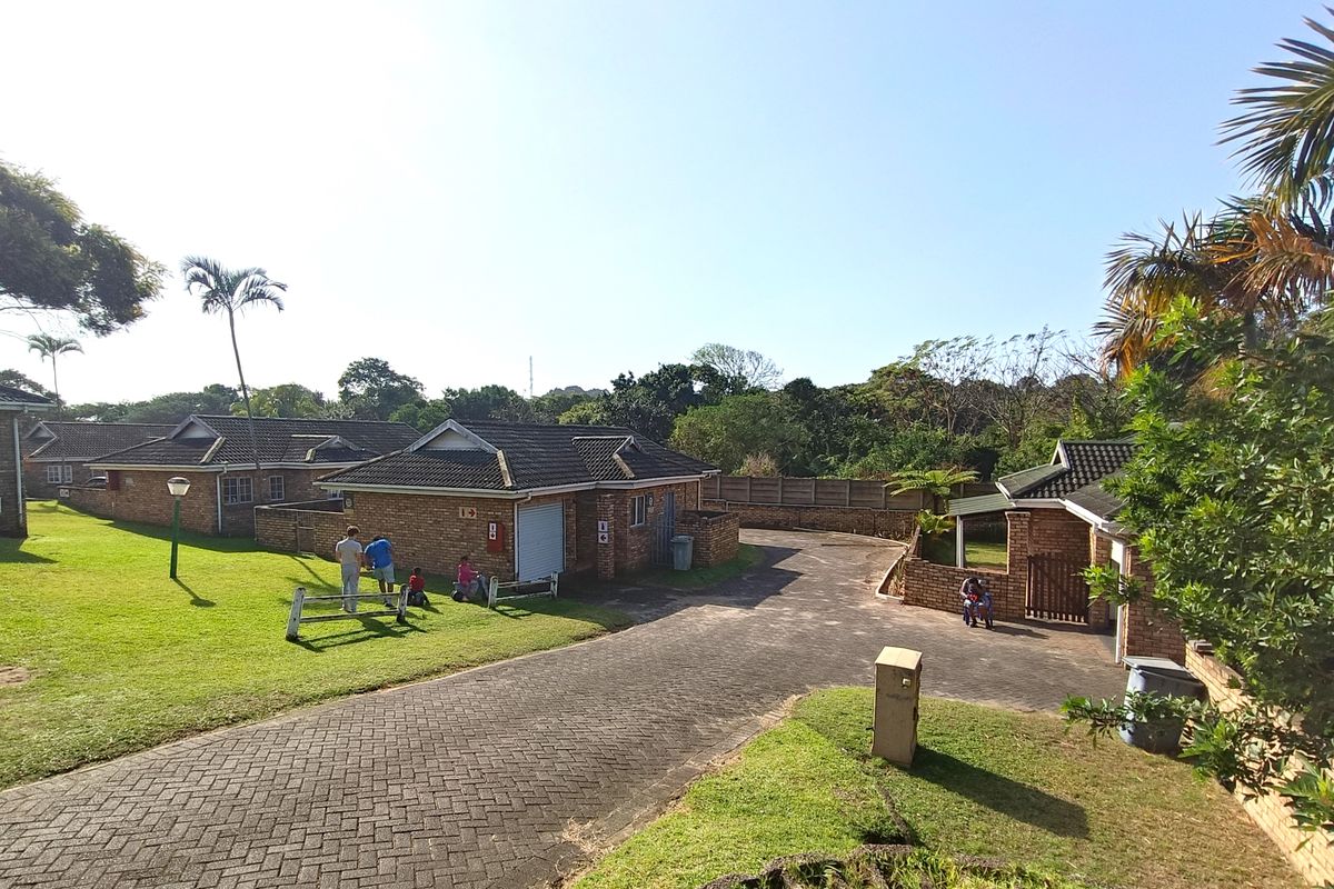 Exterior view of a townhouse complex featuring facebrick buildings, tiled roofs, and paved driveway areas set within a landscaped communal garden.