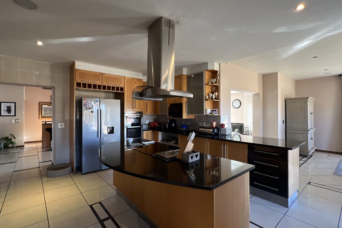 Spacious kitchen featuring a central island with granite countertops, stainless steel extractor fan, built-in oven, and tiled flooring throughout.