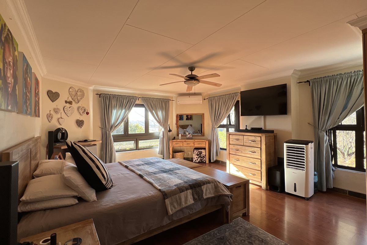 Spacious bedroom featuring laminate flooring, a ceiling fan, and a wall-mounted air conditioning unit, offering a comfortable and well-maintained living space.