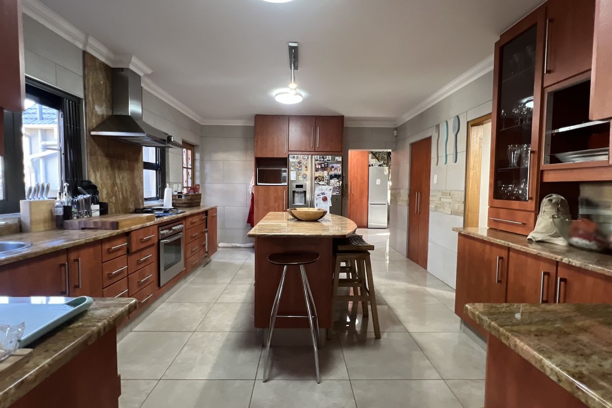Spacious kitchen featuring extensive wooden cabinetry, granite countertops, a central island, and integrated appliances with neutral tiled flooring.