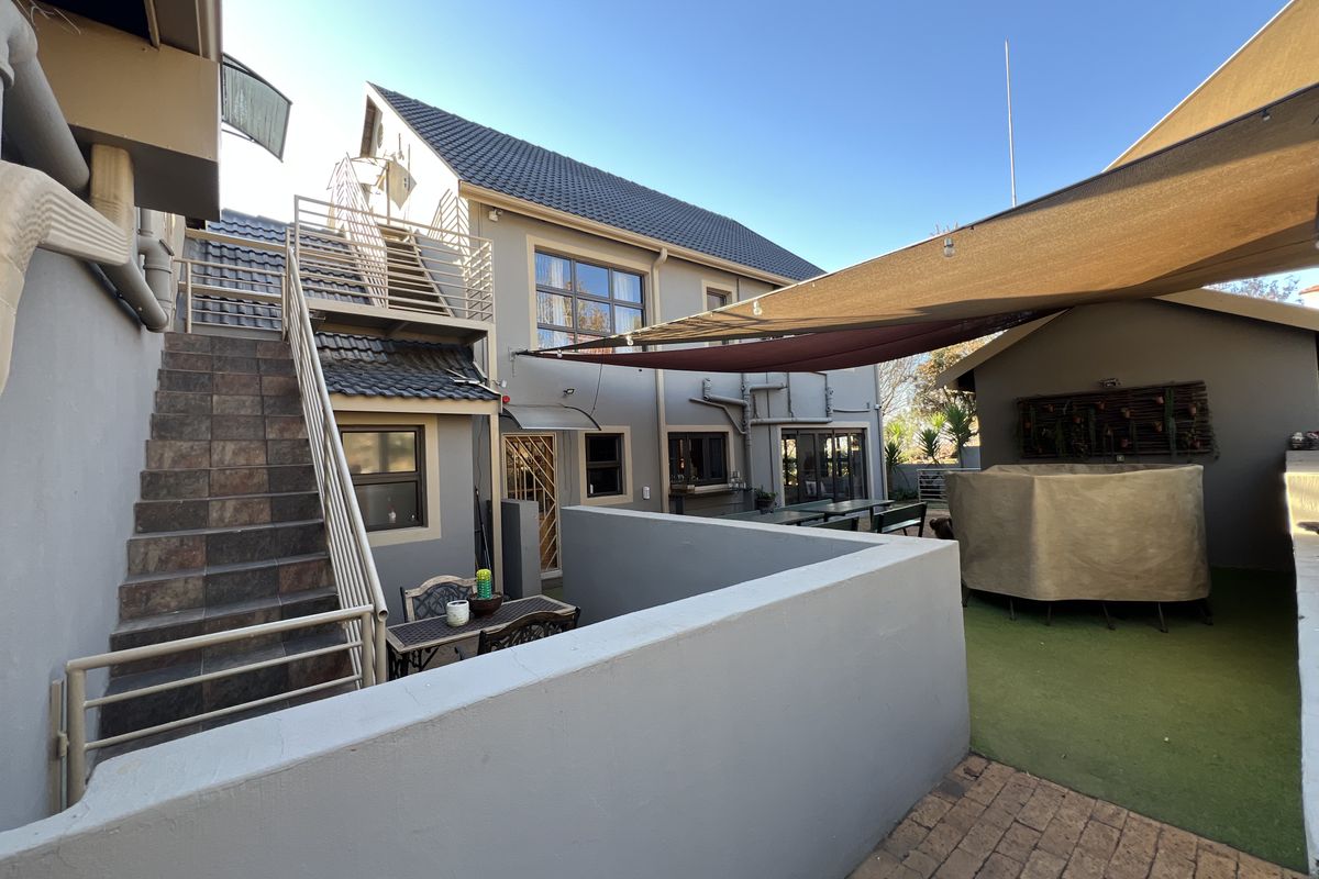 Rear exterior view featuring a tiled staircase, artificial lawn area, and a shade sail covering the outdoor entertainment space.