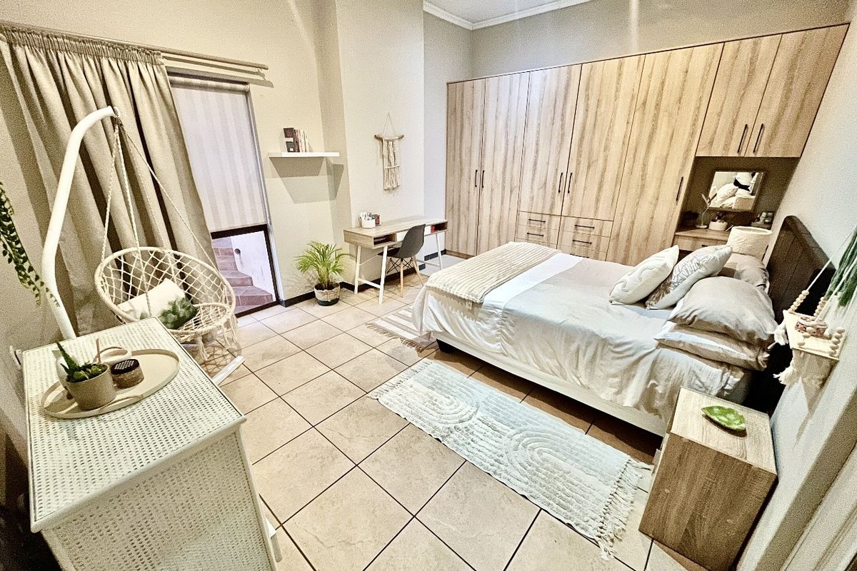 Spacious bedroom featuring neutral tiled flooring, extensive built-in wooden cabinetry, and direct access to an outdoor area through a sliding door.