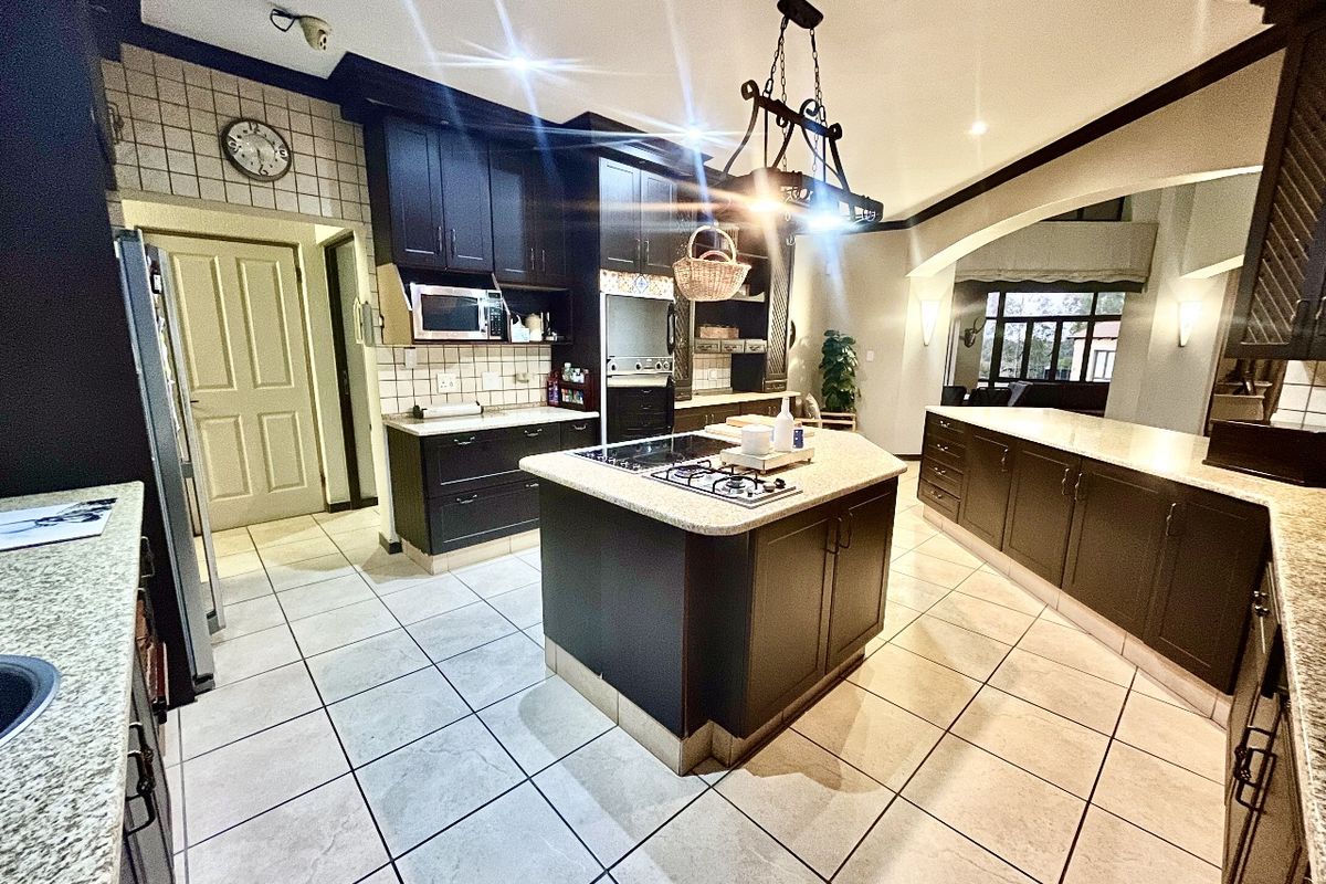 Spacious kitchen featuring dark cabinetry, granite countertops, a central island with a gas hob, and tiled flooring, offering a functional and well-defined cooking space.
