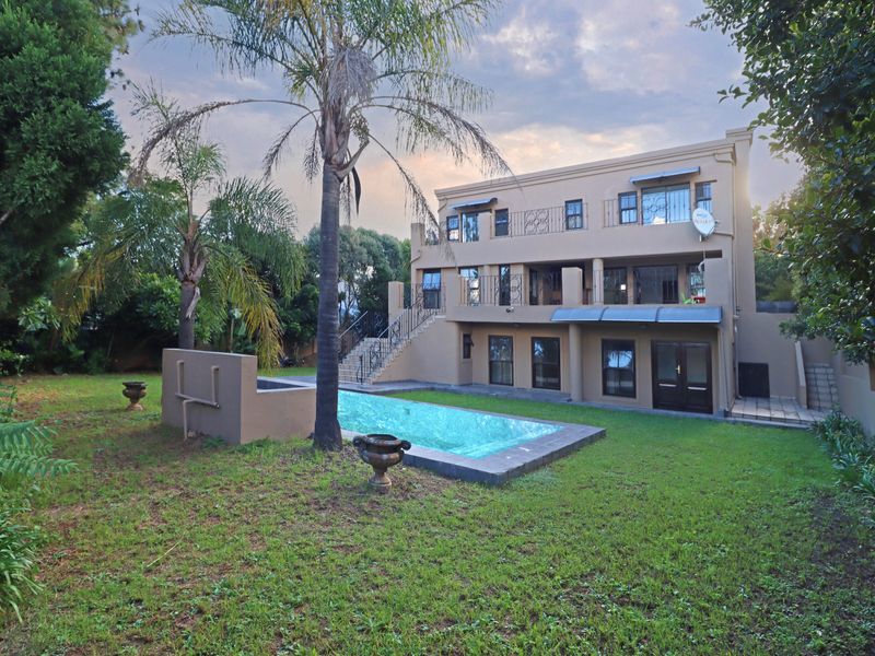 Rear view of a multi-story house featuring a swimming pool, landscaped garden, covered patio, and wrought iron balcony railings.