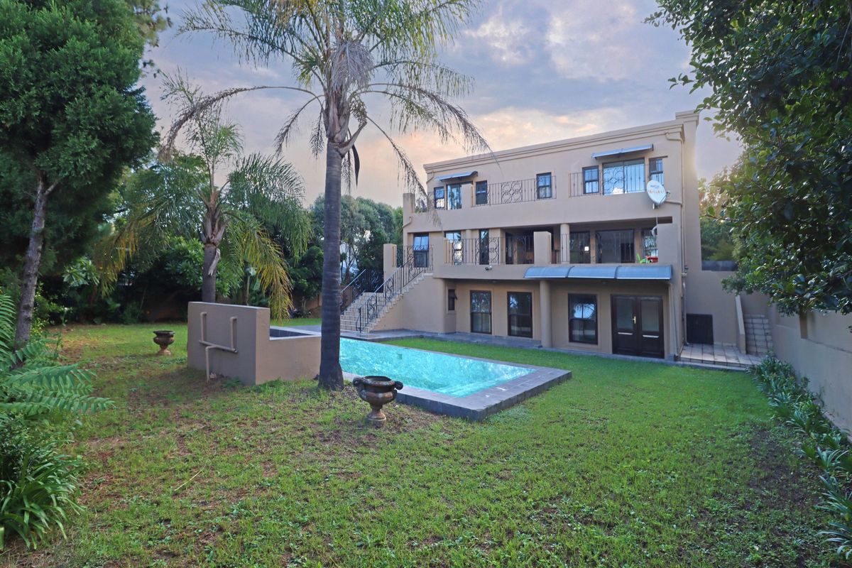 Rear view of a multi-story house featuring a swimming pool, landscaped garden, covered patio, and wrought iron balcony railings.