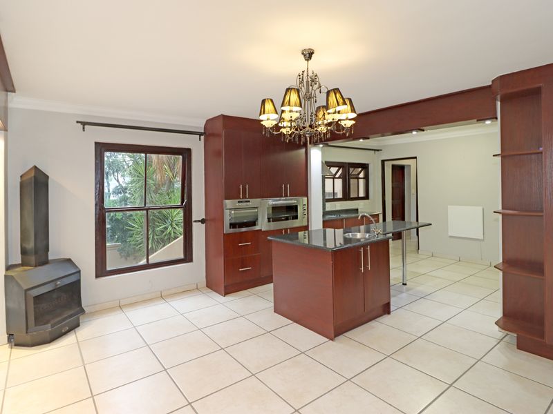 Spacious kitchen featuring dark wood cabinetry, granite countertops, a central island with sink, built-in appliances, and a cozy fireplace in an open-plan layout.