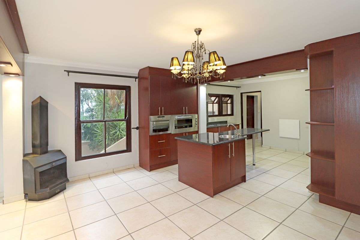 Spacious kitchen featuring dark wood cabinetry, granite countertops, a central island with sink, built-in appliances, and a cozy fireplace in an open-plan layout.