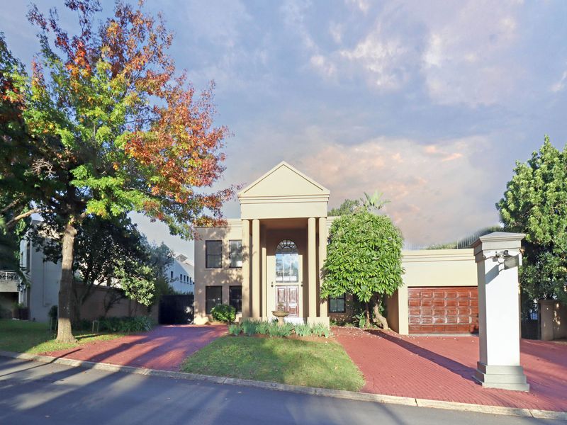 A well-maintained double-story residence featuring a grand portico entrance, arched architectural detailing, and a paved driveway leading to a double garage.