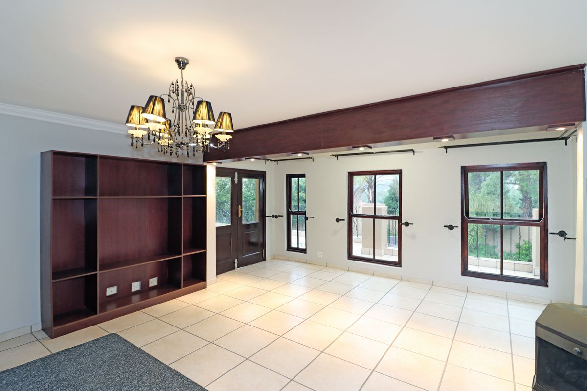 Spacious living area featuring tiled flooring, built-in wooden shelving, decorative chandelier, and large timber-framed windows providing natural light and access to the exterior.