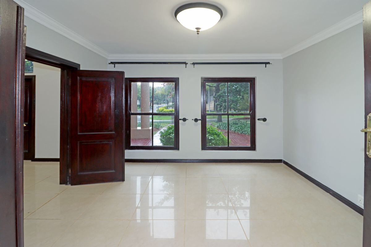 A bright, empty bedroom featuring polished tile flooring, dark wood door and window frames, and crown molding, offering a clean and neutral living space.