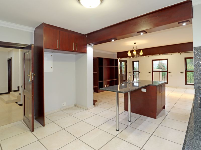 Spacious open-plan kitchen and living area featuring granite countertops, a central island, built-in cabinetry, and neutral ceramic floor tiles throughout.