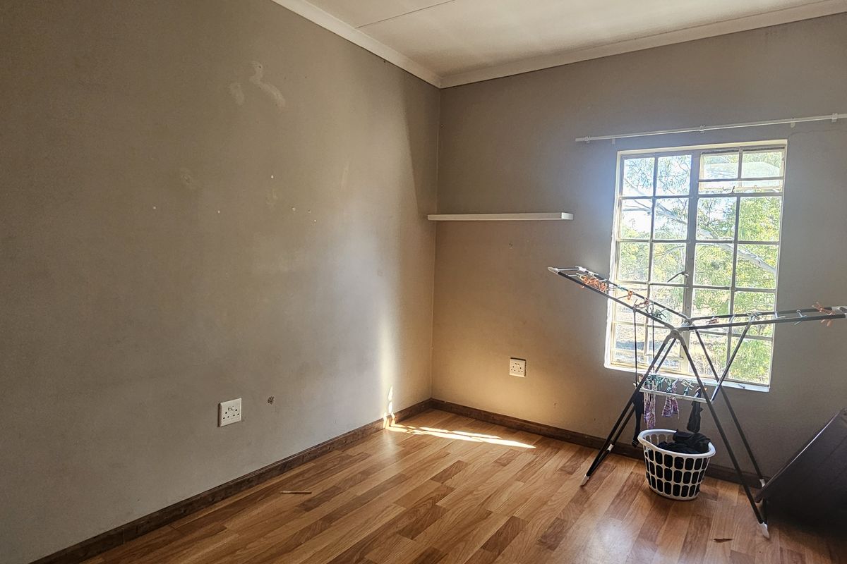A vacant bedroom featuring laminate flooring and a window, requiring minor cosmetic updates to the wall surfaces.
