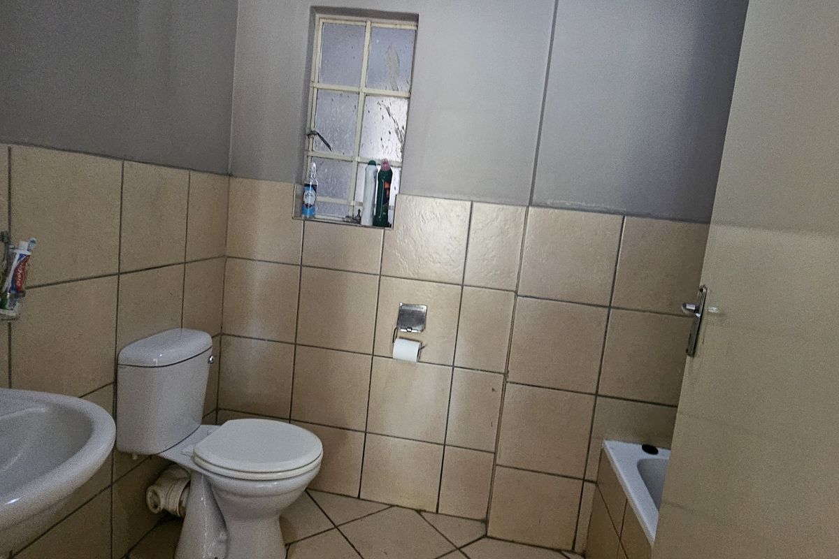 A functional bathroom featuring a pedestal basin, toilet, and bathtub with neutral ceramic tiling throughout, requiring some cosmetic updates to improve its overall condition.