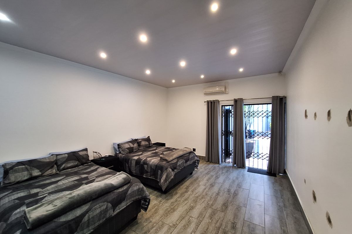 Spacious bedroom featuring tiled flooring, recessed downlighting, a split-system air conditioner, and direct access to an outdoor area through a secure sliding glass door.