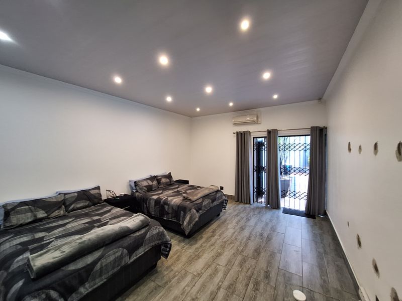 Spacious bedroom featuring tiled flooring, recessed downlighting, a split-system air conditioner, and direct access to an outdoor area through a secure sliding glass door.