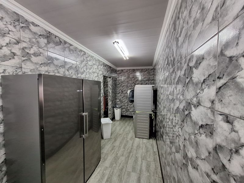 A functional laundry room featuring full-height marble-effect wall tiling, wood-look floor tiles, and efficient overhead lighting.