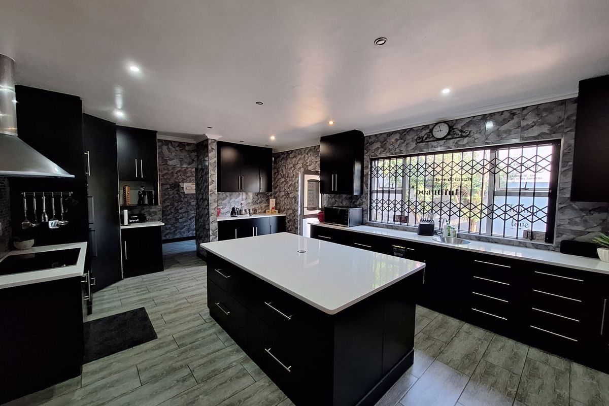 Modern kitchen featuring a central island with quartz countertops, dark cabinetry, wood-look tile flooring, and a stainless steel sink.