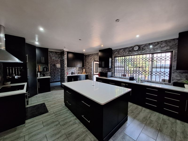 Modern kitchen featuring a central island with quartz countertops, dark cabinetry, wood-look tile flooring, and a stainless steel sink.