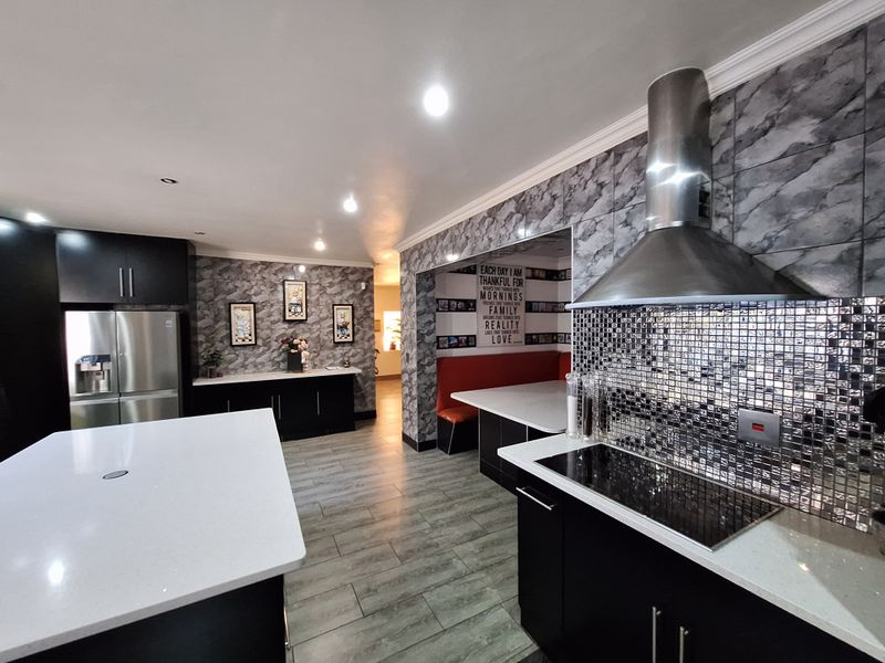Modern kitchen featuring a large island, quartz countertops, sleek black cabinetry, stainless steel extractor fan, and a stylish mosaic tile backsplash.