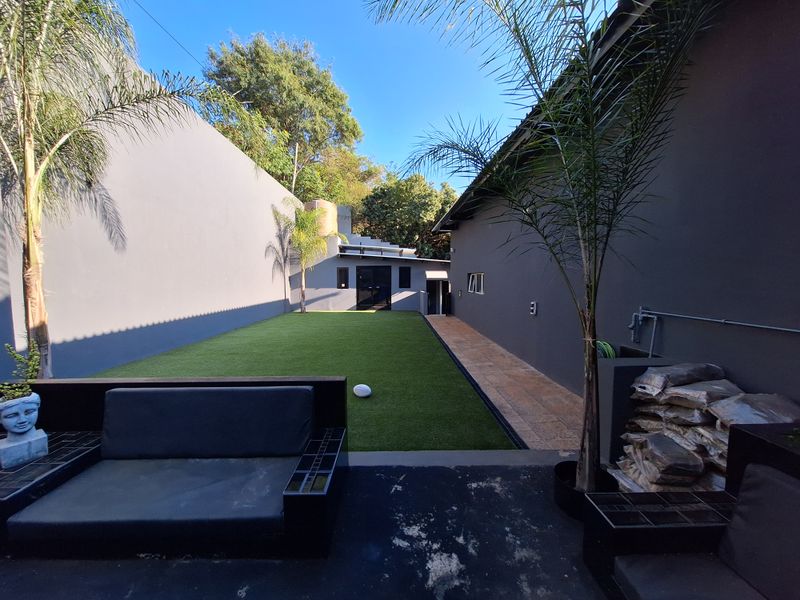 A private rear garden featuring a level artificial lawn, tiled side walkway, and high boundary walls, providing a low-maintenance outdoor space.