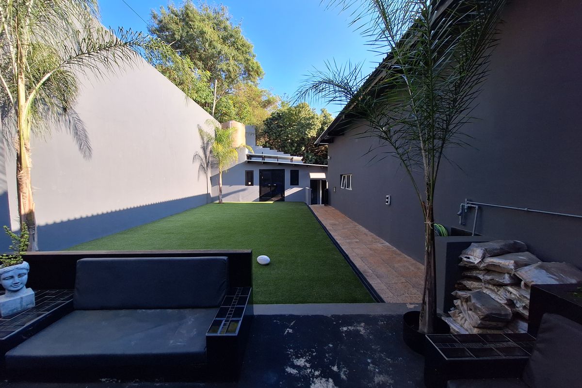 A private rear garden featuring a level artificial lawn, tiled side walkway, and high boundary walls, providing a low-maintenance outdoor space.