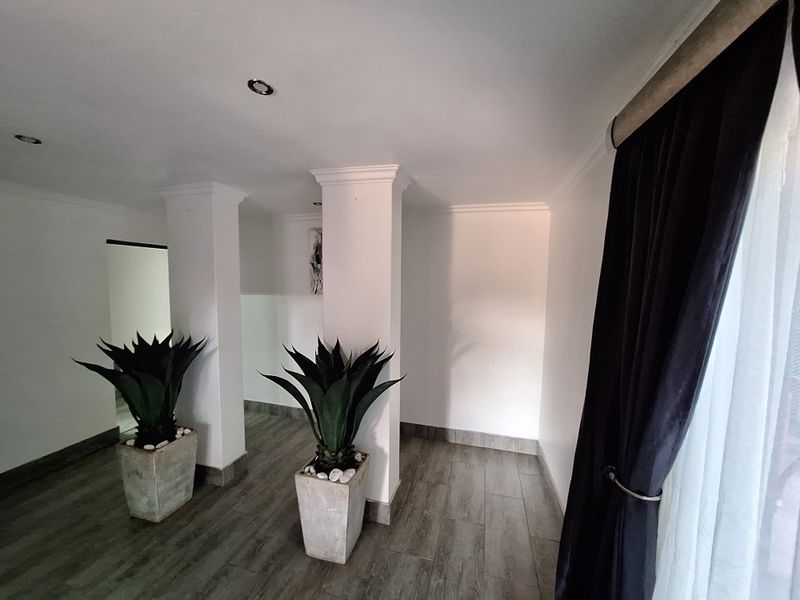 A bright and spacious living area featuring neutral walls, tiled flooring, crown molding, and structural columns, offering a clean and modern aesthetic.