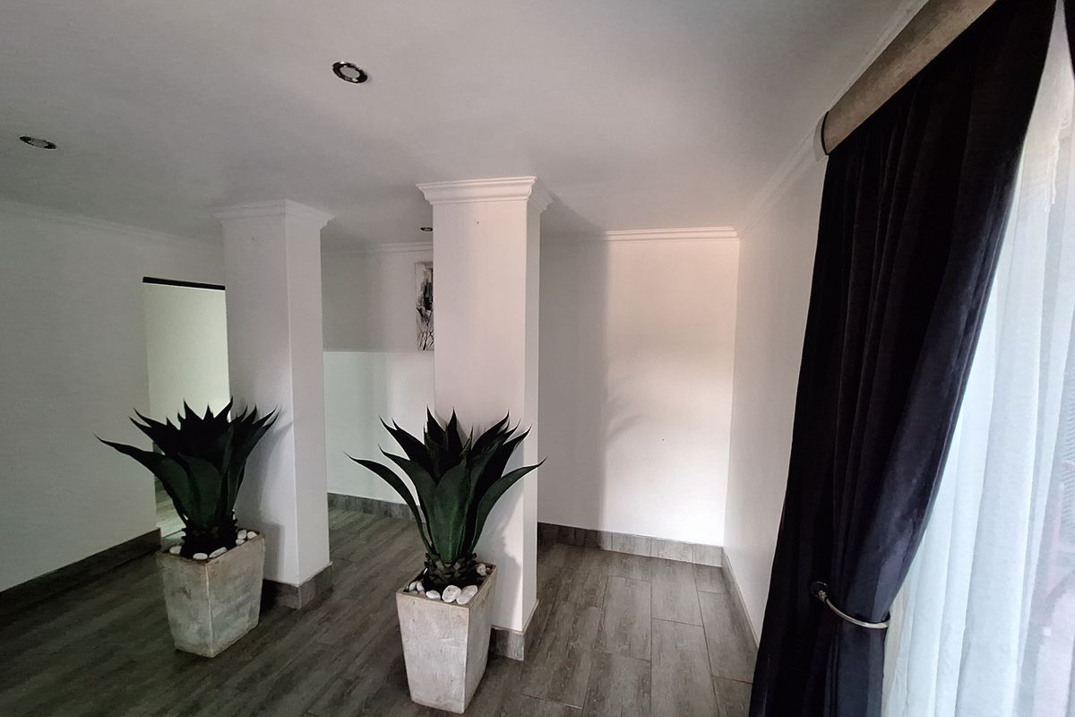 A bright and spacious living area featuring neutral walls, tiled flooring, crown molding, and structural columns, offering a clean and modern aesthetic.