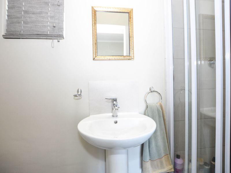 A functional bathroom featuring a pedestal basin with chrome mixer tap and a glass-enclosed shower with tiled walls.
