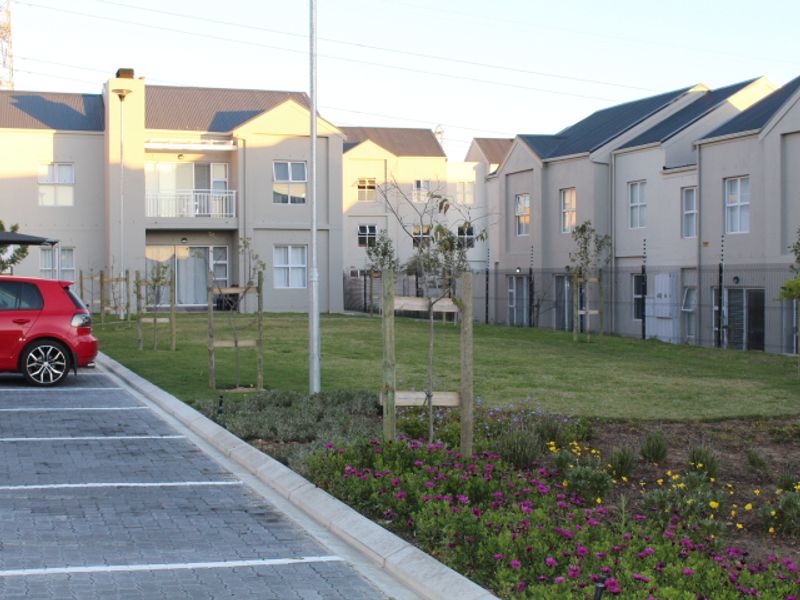 View of the apartment complex rear elevation featuring a communal garden, paved parking area, and modern building architecture with balconies.
