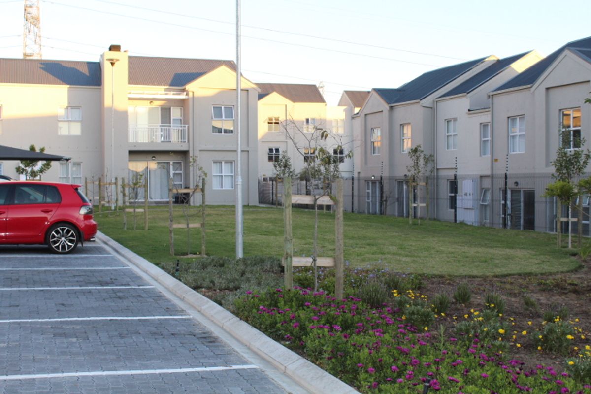 View of the apartment complex rear elevation featuring a communal garden, paved parking area, and modern building architecture with balconies.