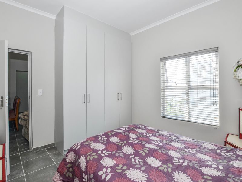 A well-maintained bedroom featuring neutral walls, tiled flooring, a large built-in wardrobe, and a window fitted with venetian blinds.