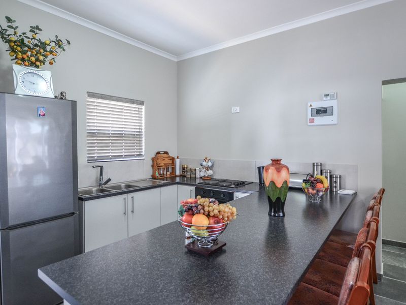 A functional kitchen featuring dark laminate countertops, built-in cabinetry, a stainless steel sink, and a built-in hob with an integrated breakfast bar.
