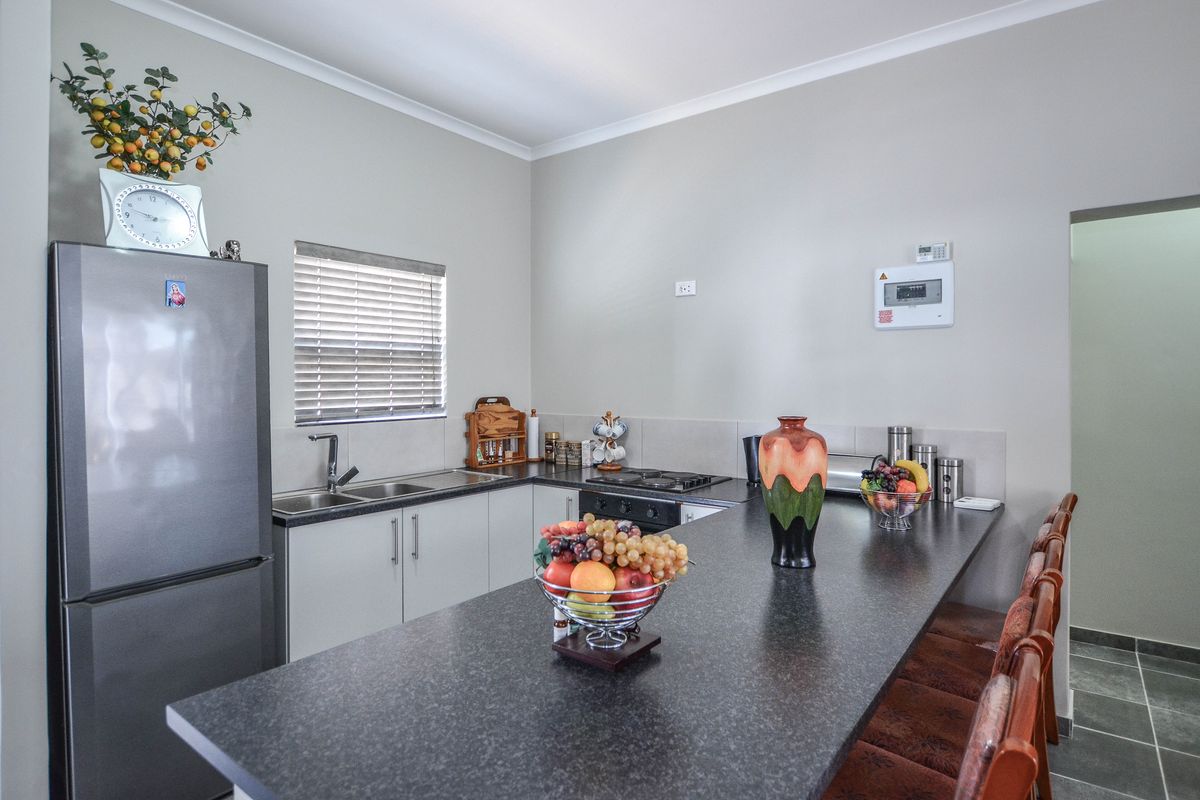A functional kitchen featuring dark laminate countertops, built-in cabinetry, a stainless steel sink, and a built-in hob with an integrated breakfast bar.