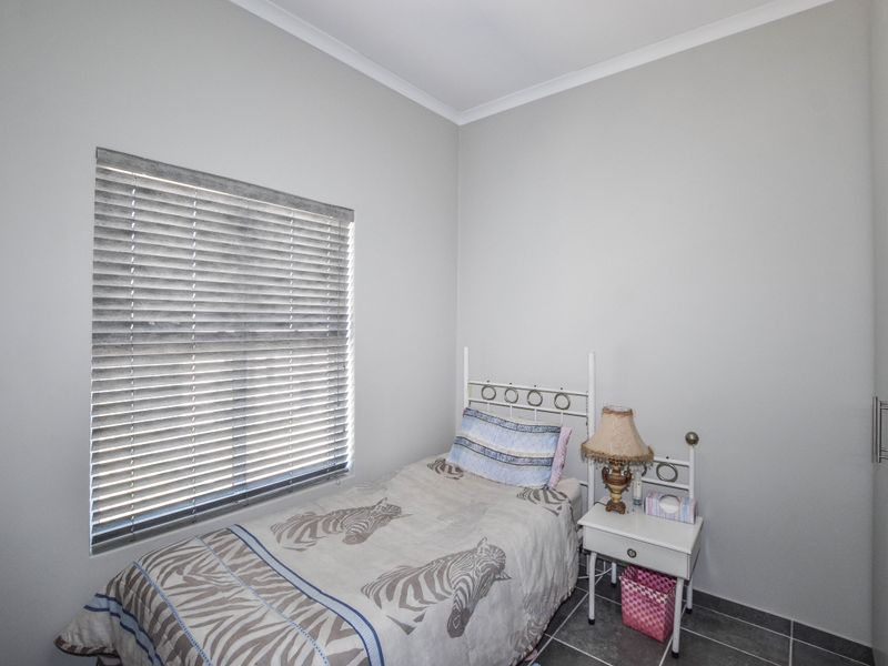 A compact bedroom featuring neutral wall finishes, tiled flooring, built-in cupboard storage, and venetian blinds for light control.