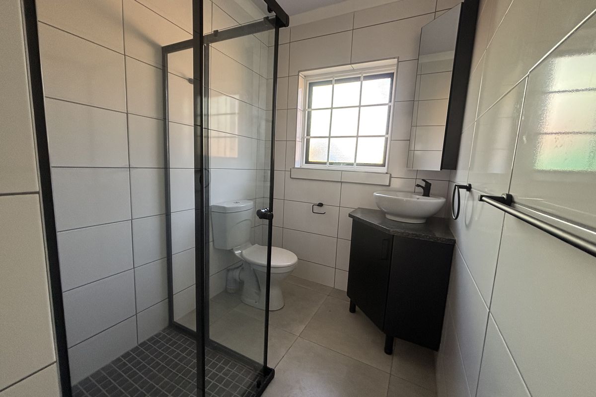 A modern bathroom featuring a glass-enclosed shower, a vessel sink vanity, and neutral wall tiling.