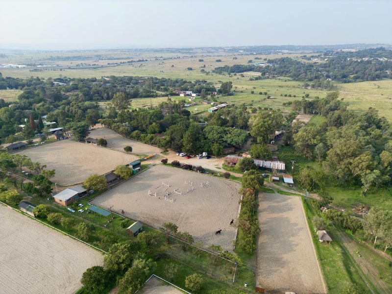 Aerial view of a farm property featuring multiple equestrian arenas, outbuildings, and expansive surrounding landscape.
