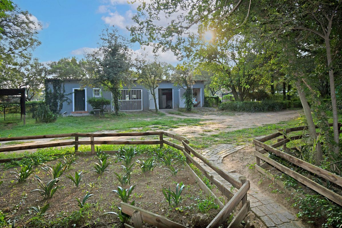 Exterior view of a farm outbuilding featuring multiple access points, surrounded by a landscaped garden area with timber fencing and mature trees.