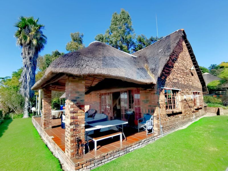 A charming farm-style cottage featuring a traditional thatched roof, exposed brick exterior, and a spacious covered patio overlooking the surrounding garden.