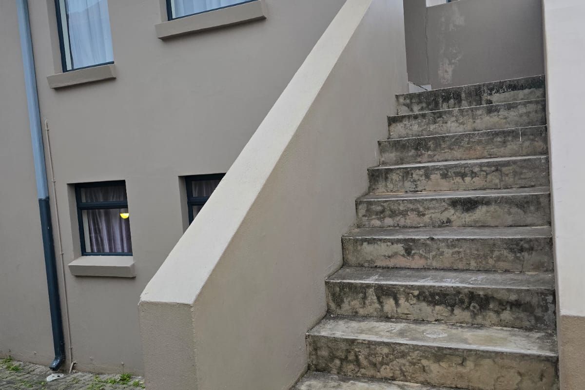 Exterior view of a townhouse featuring a concrete staircase leading to an upper level, set against a paved courtyard area.