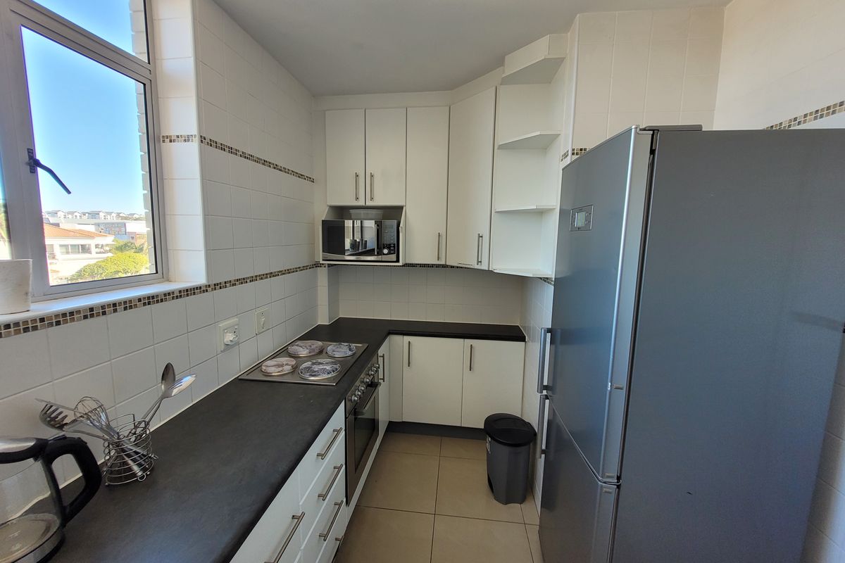 A functional kitchen featuring white cabinetry, dark countertops, built-in appliances, and tiled finishes, offering a clean and practical workspace.
