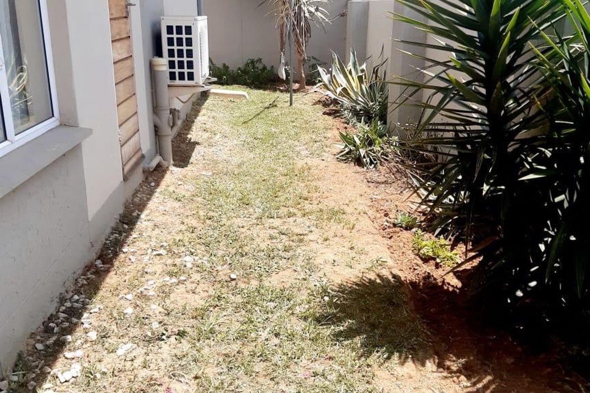 A narrow rear garden area featuring a lawn, boundary wall, and an external air conditioning unit mounted on the side of the townhouse.