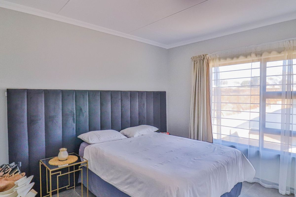 A well-lit bedroom featuring neutral wall finishes, coving, and security bars on the window.