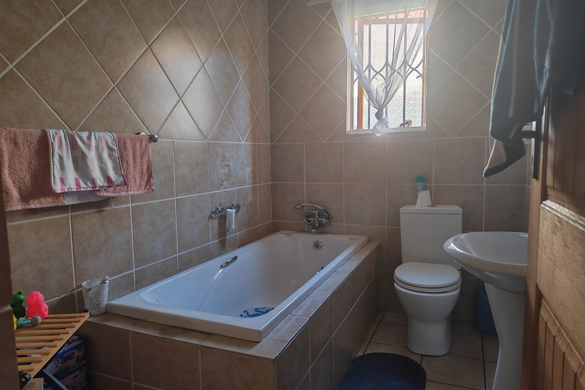 A functional bathroom featuring a built-in bathtub, pedestal basin, toilet, and full-height ceramic wall tiling.