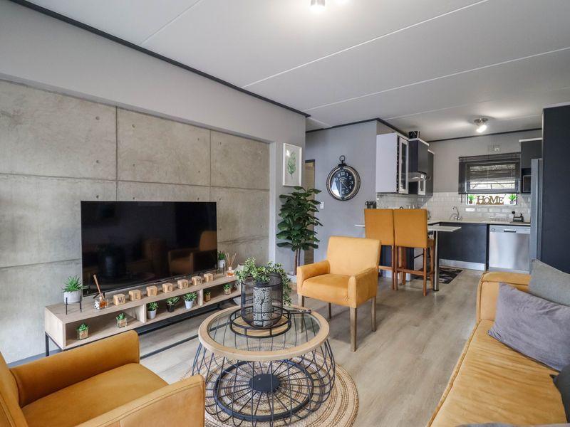 Modern open-plan living area featuring a concrete accent wall, laminate flooring, and a functional kitchen with a breakfast bar and subway tile backsplash.