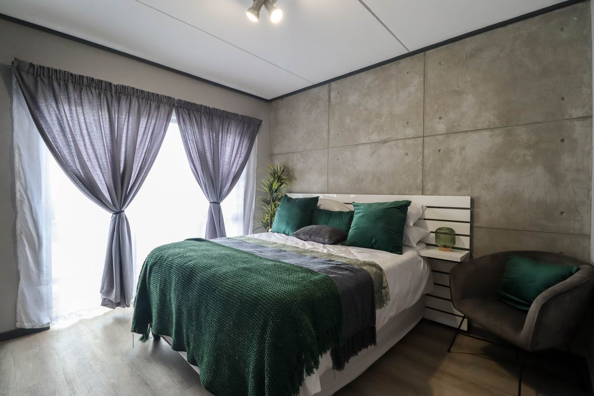 A modern bedroom featuring a concrete panel feature wall, laminate flooring, and large windows with curtains.